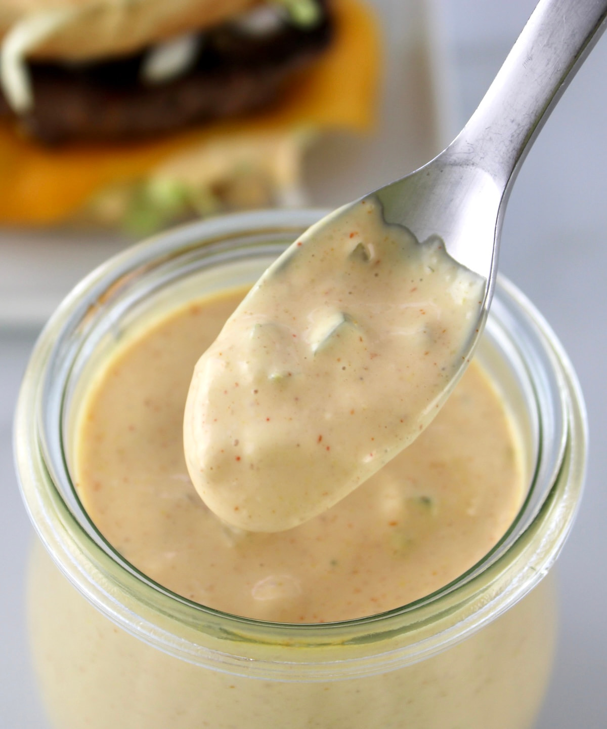 closeup of Keto Big Mac Sauce being spooned out of glass jar wiht burger in back