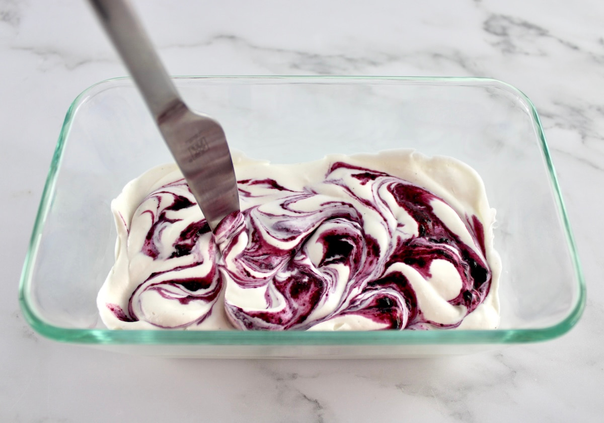 knife swirling through dollops of blueberry sauce in vanilla ice cream