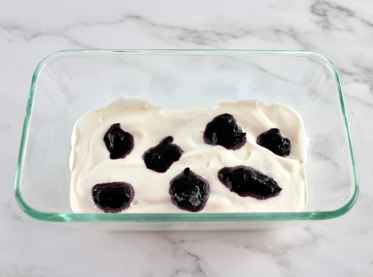 vanilla ice cream base with dollops of blueberry sauce on top in glass loaf pan