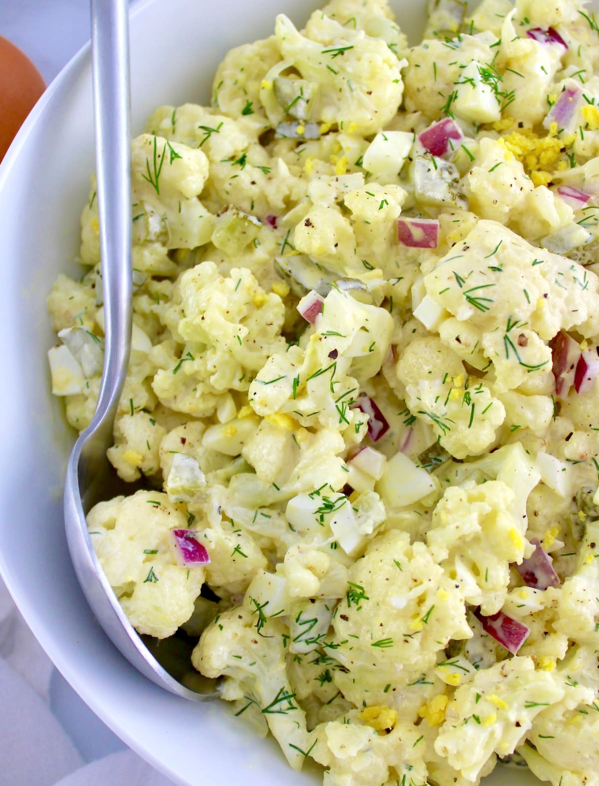 closeup of Cauliflower Potato Salad in white bowl with serving spoon