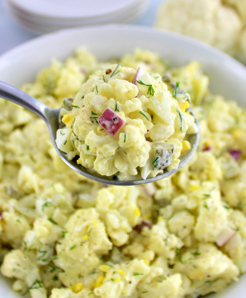 Cauliflower Potato Salad in spoon held up over white bowl