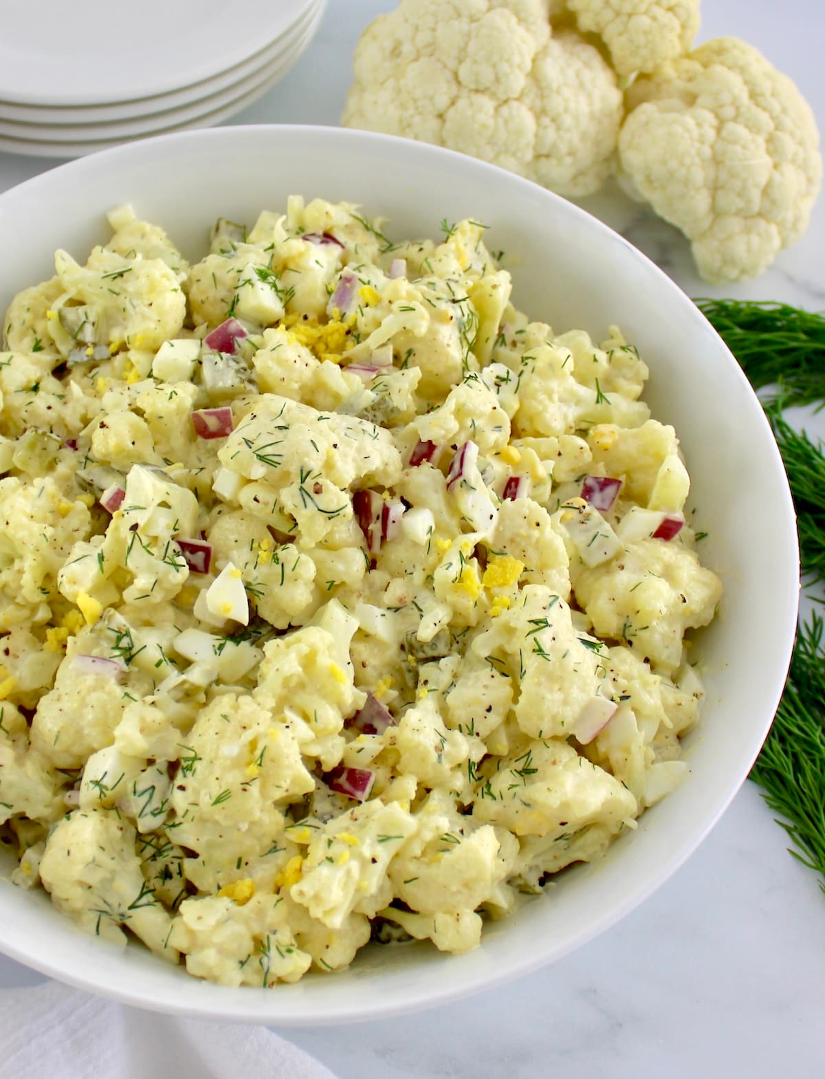 Cauliflower Potato Salad in white bowl with cauliflower and small plates in back
