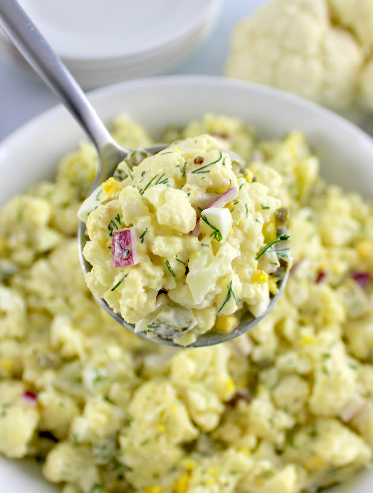 spoonful of Cauliflower Potato Salad held up over white bowl