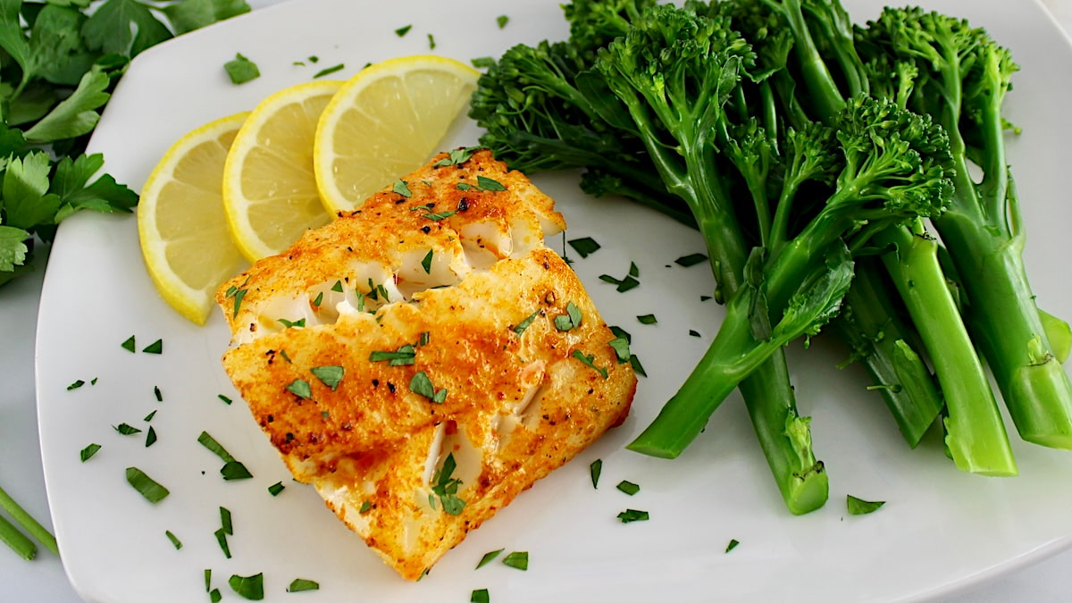 Easy Air Fryer Cod on white plate with broccolini and lemon slices on side