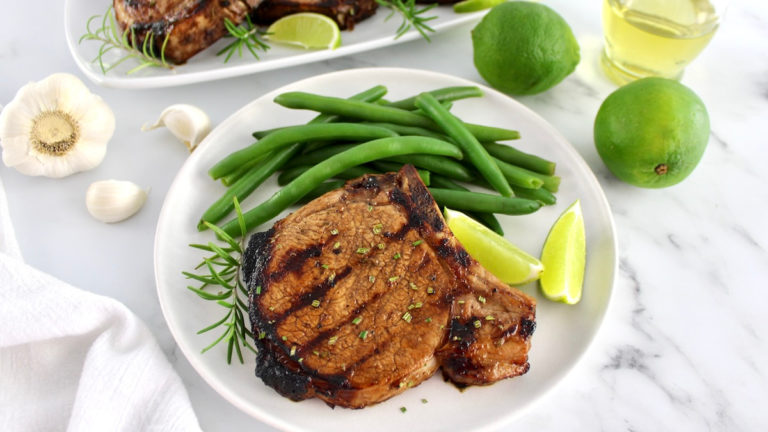 Grilled pork chop on white plate with green beans and lime wedges