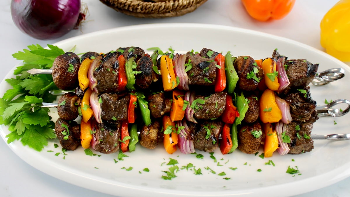 grilled beef kebabs on white plate with parsley garnish