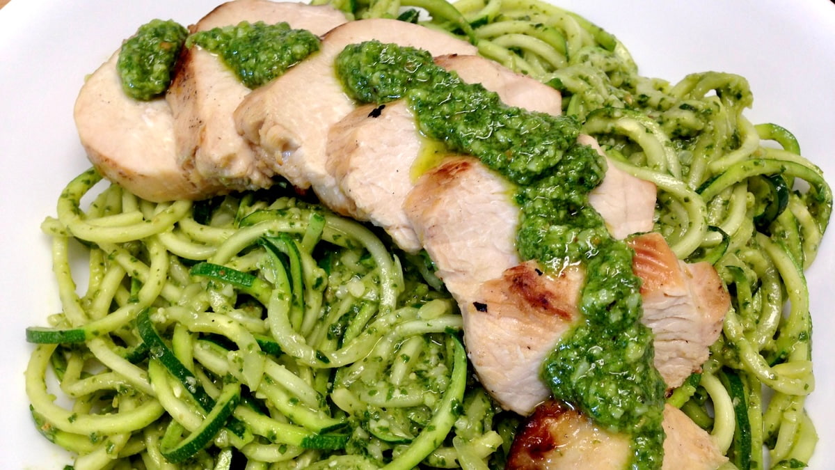 sliced lemon chicken with pesto sauce over zucchini noodles