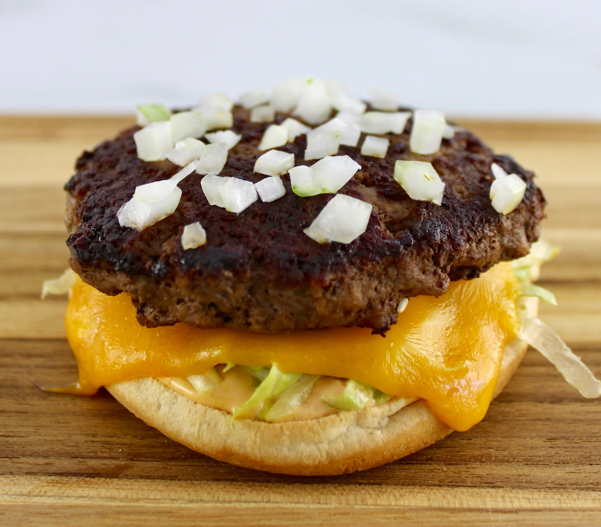 hamburger patty with diced onions cheese and lettuce on bun bottom