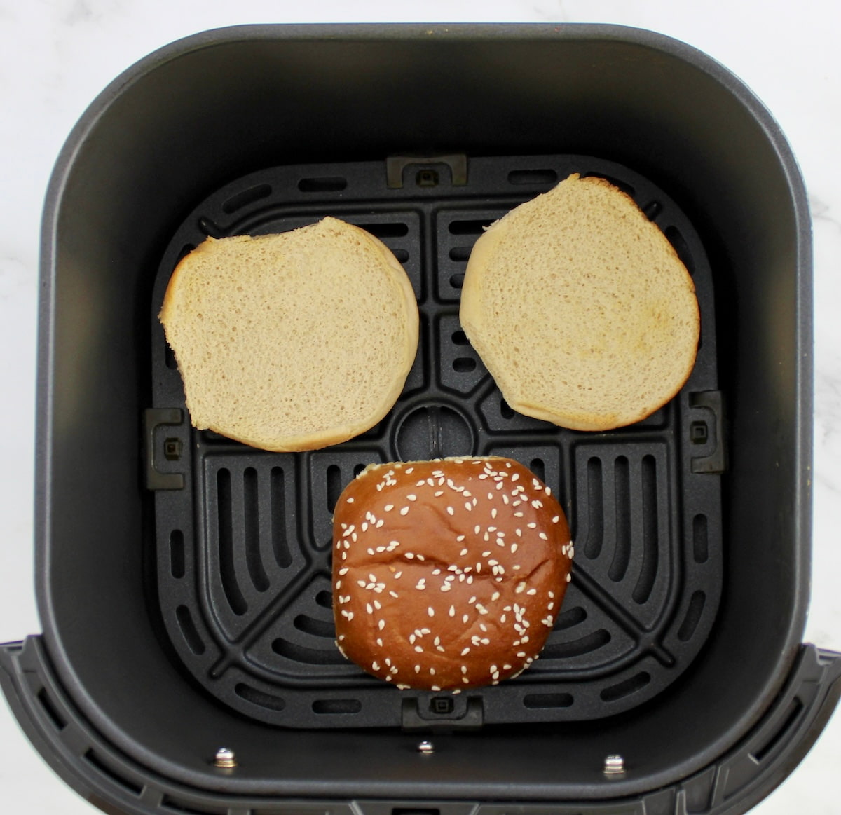 1 top hamburger bun and 2 bottom buns in air fryer basket