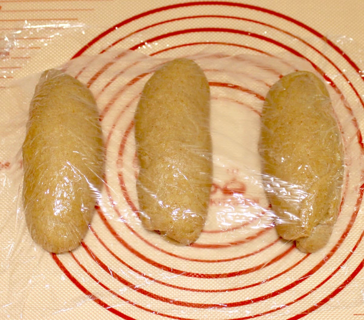3 logs of Keto Brioche Bread dough on Silpat covered with plastic wrap