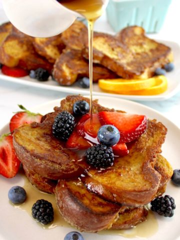 Keto French Toast on white plate with fresh berries and maple syrup being poured on top