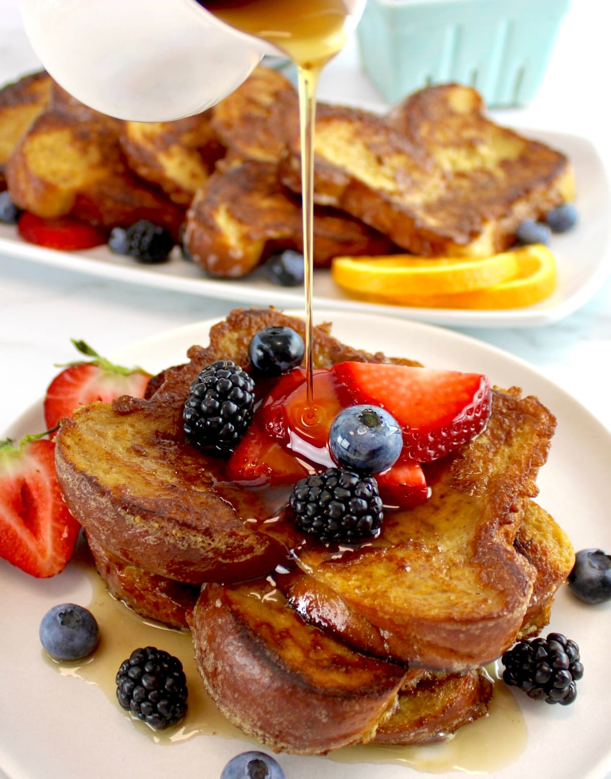 Keto French Toast on white plate with fresh berries and maple syrup being poured on top