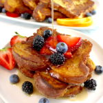 Keto French Toast on white plate with fresh berries and maple syrup being poured on top