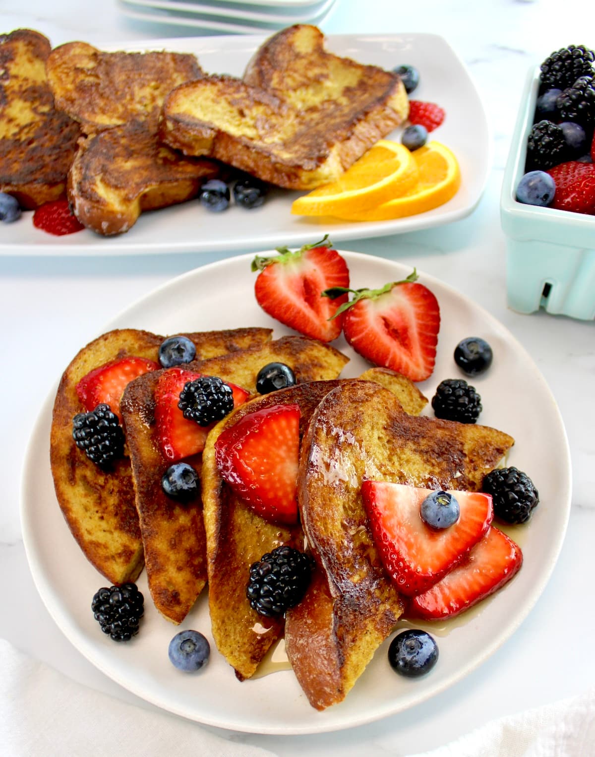 overhead view of 4 triangles of Keto French Toast on white palte with fresh berries around