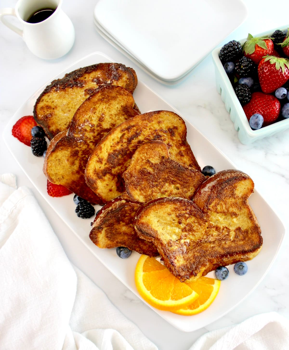 overhead view of 5 slices of Keto French Toast on white plate with berries and orange slices on side