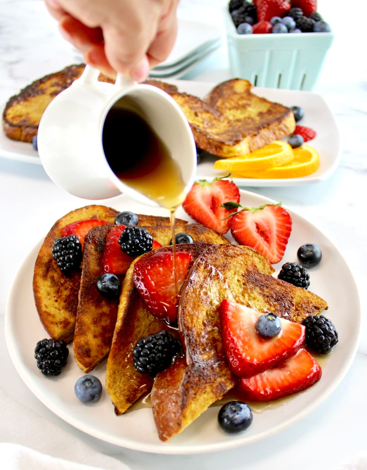 maple syrup being poured over 4 triangles of Keto French Toast on white plate with berries