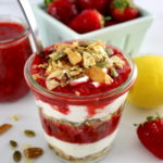 Keto Strawberry Granola Parfait in glass jar with spoon and strawberries in back