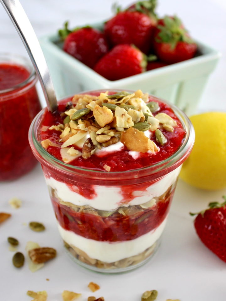 Keto Strawberry Granola Parfait in glass jar with spoon and strawberries in back