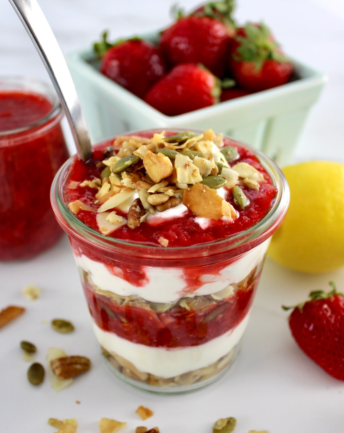 Keto Strawberry Granola Parfait in glass jar with spoon and strawberries in back