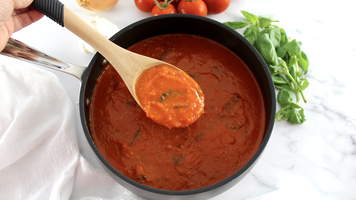 roasted tomato sauce in skillet held up with wooden spoon