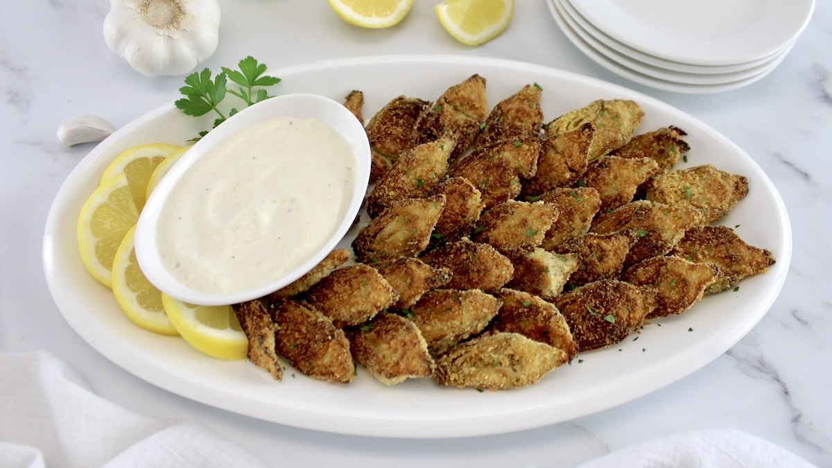 Baked Artichoke Hearts with Dipping Sauce on white oval platter with lemon slices on side