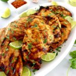 Grilled Tajin Chicken on white platted with lime slices and fresh cilantro garnish