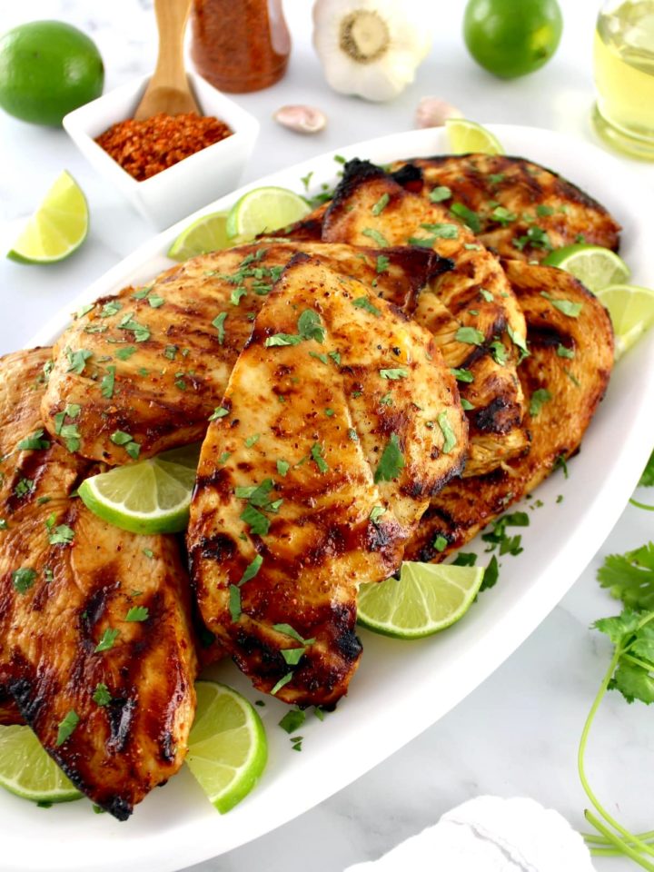 Grilled Tajin Chicken on white platted with lime slices and fresh cilantro garnish