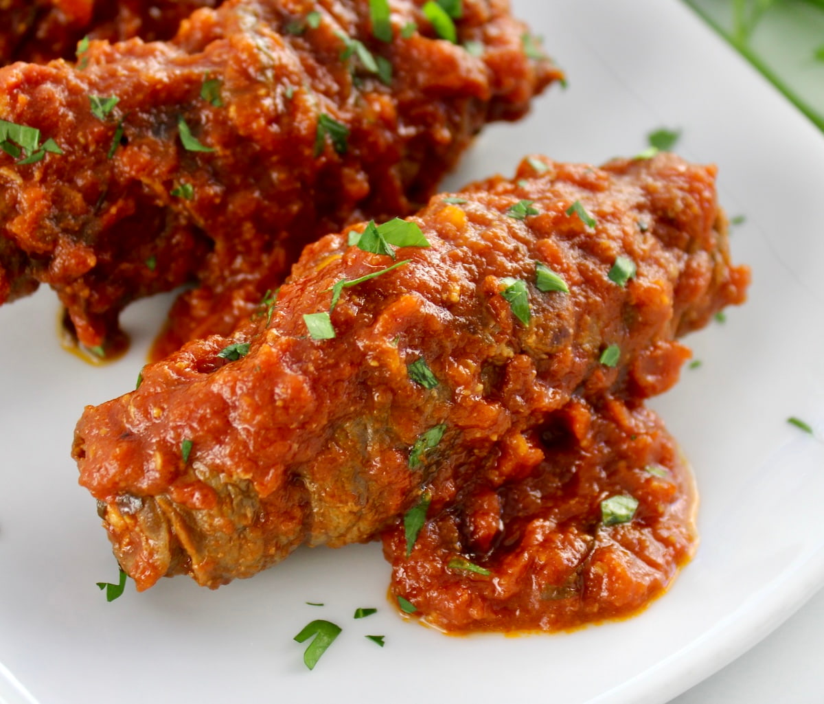 closeup of Italian Beef Braciole on white plate with parsley garnish