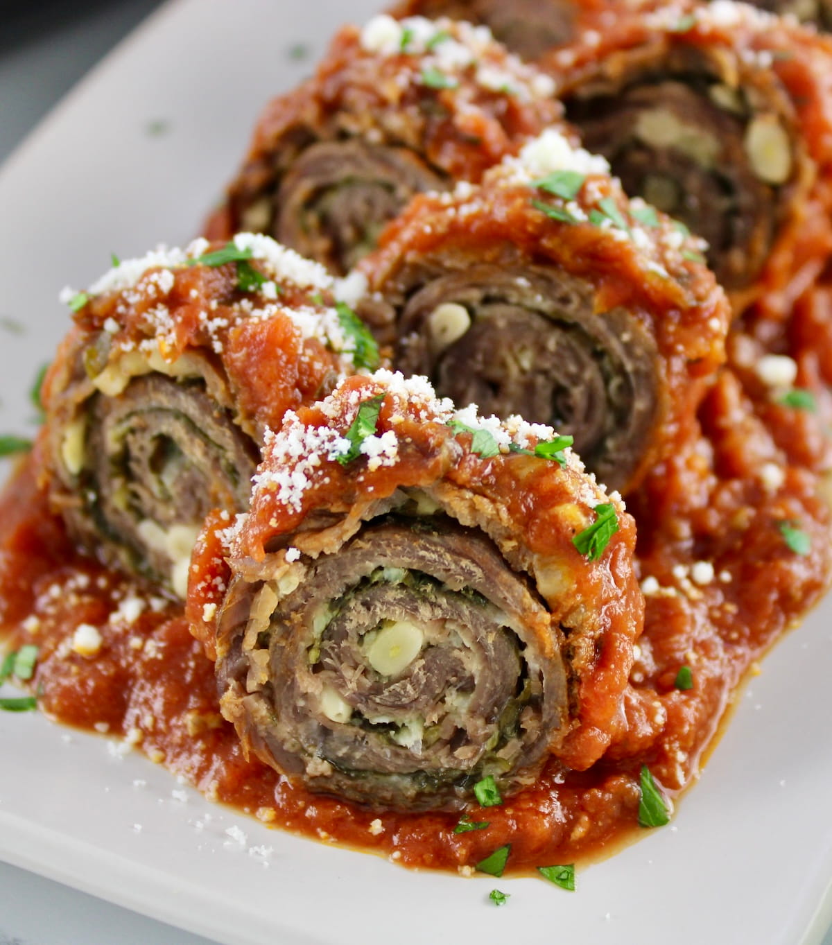 closeup of Italian Beef Braciole sliced into pinwheels on white plate with tomato sauce