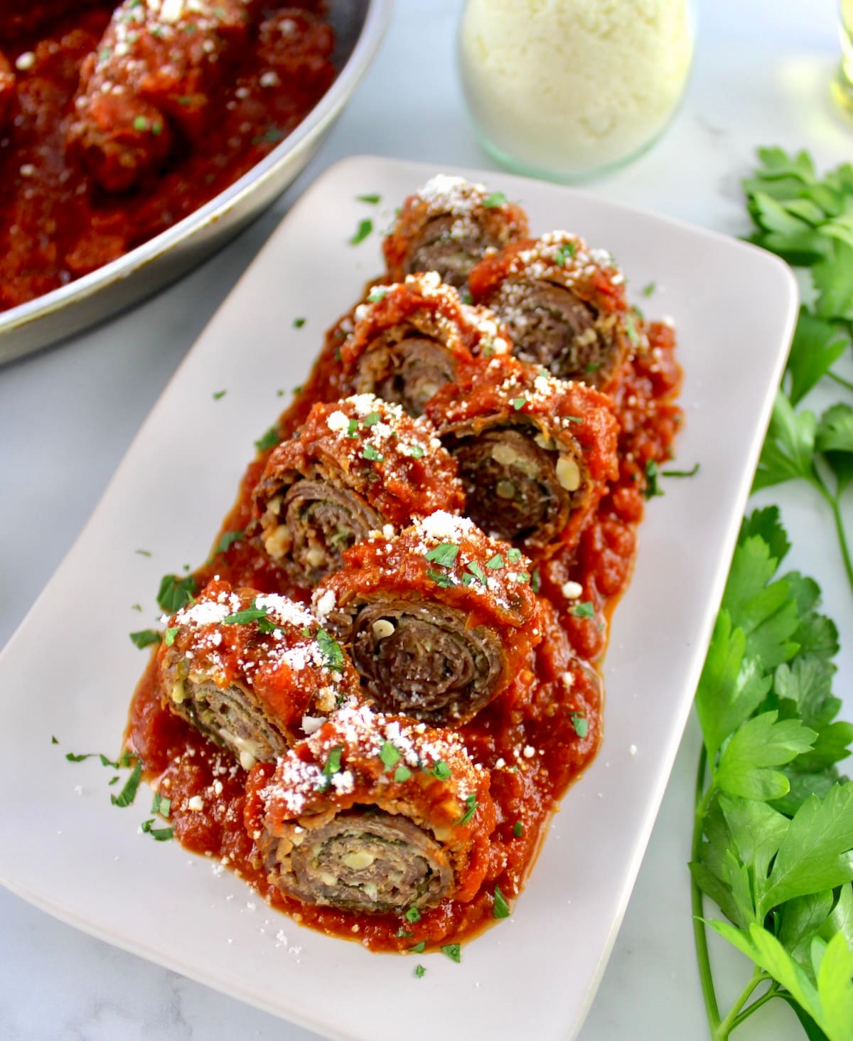 closeup of Italian Beef Braciole sliced into pinwheels on white plate with tomato sauce and parmesan cheese on top