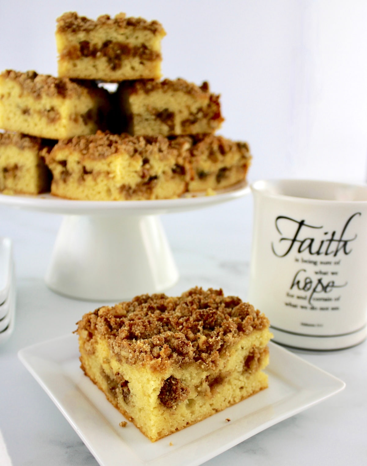 Keto Coffee Cake slice on white plate with cup of coffee and more cake in back