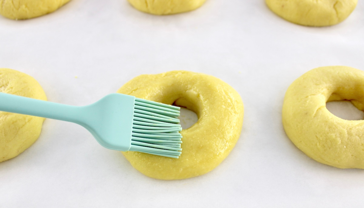 egg wash being brushed over fathead bagels on parchment paper