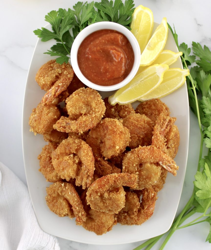 overhead view of Keto Fried Shrimp with Cocktail Sauce in white bowl with lemon wedges