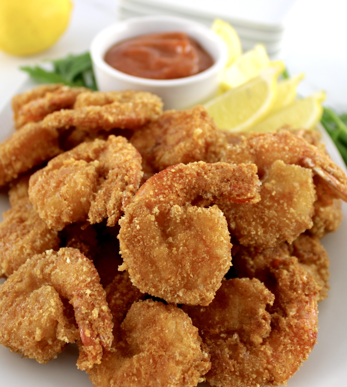 closeup of Keto Fried Shrimp with Cocktail Sauce on white plate with lemon wedges in back