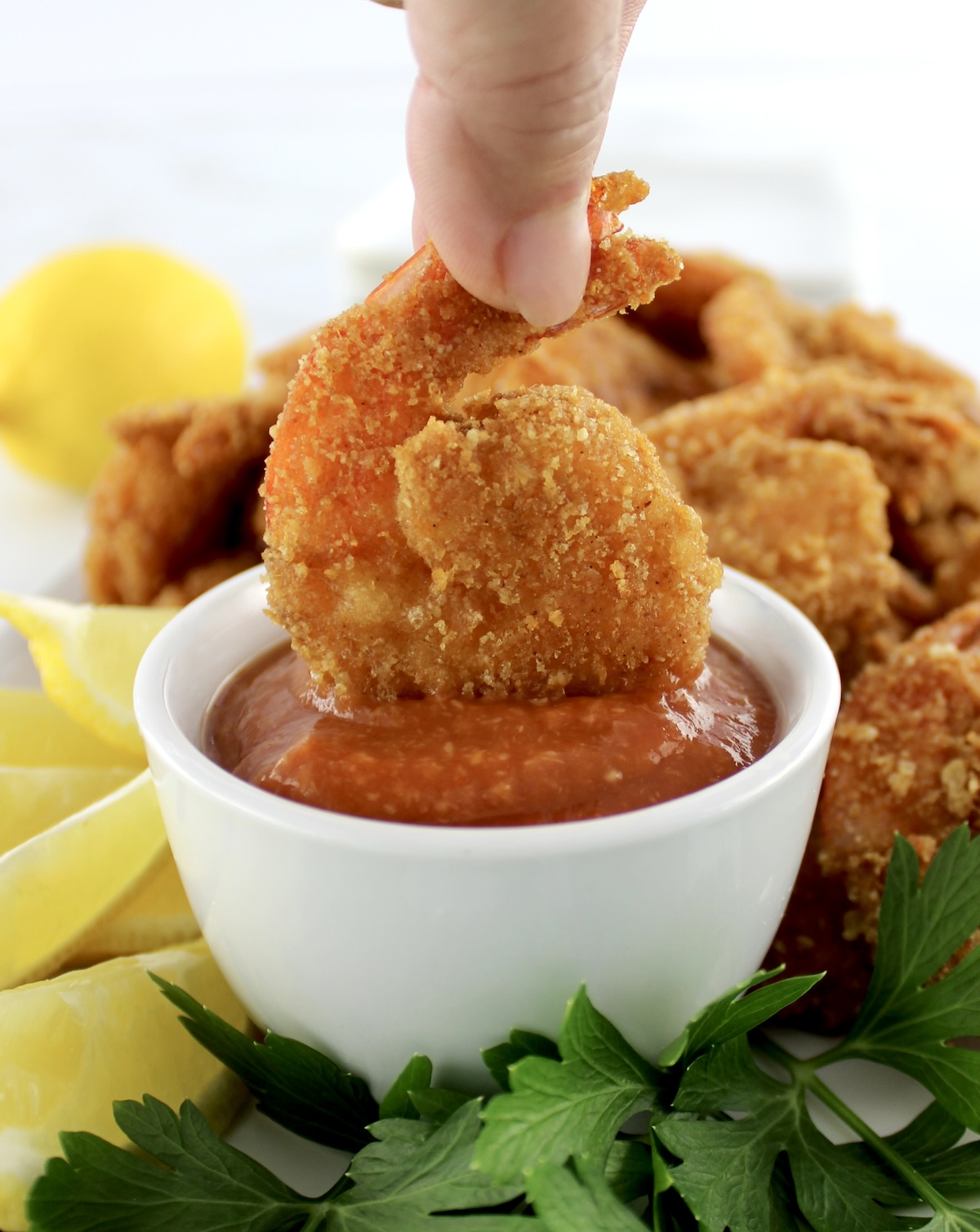 Keto Fried Shrimp being dipped into Cocktail Sauce with parsley and lemon on side