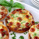 closeup of Pepperoni Pizza Bagels on white plate with fresh basil