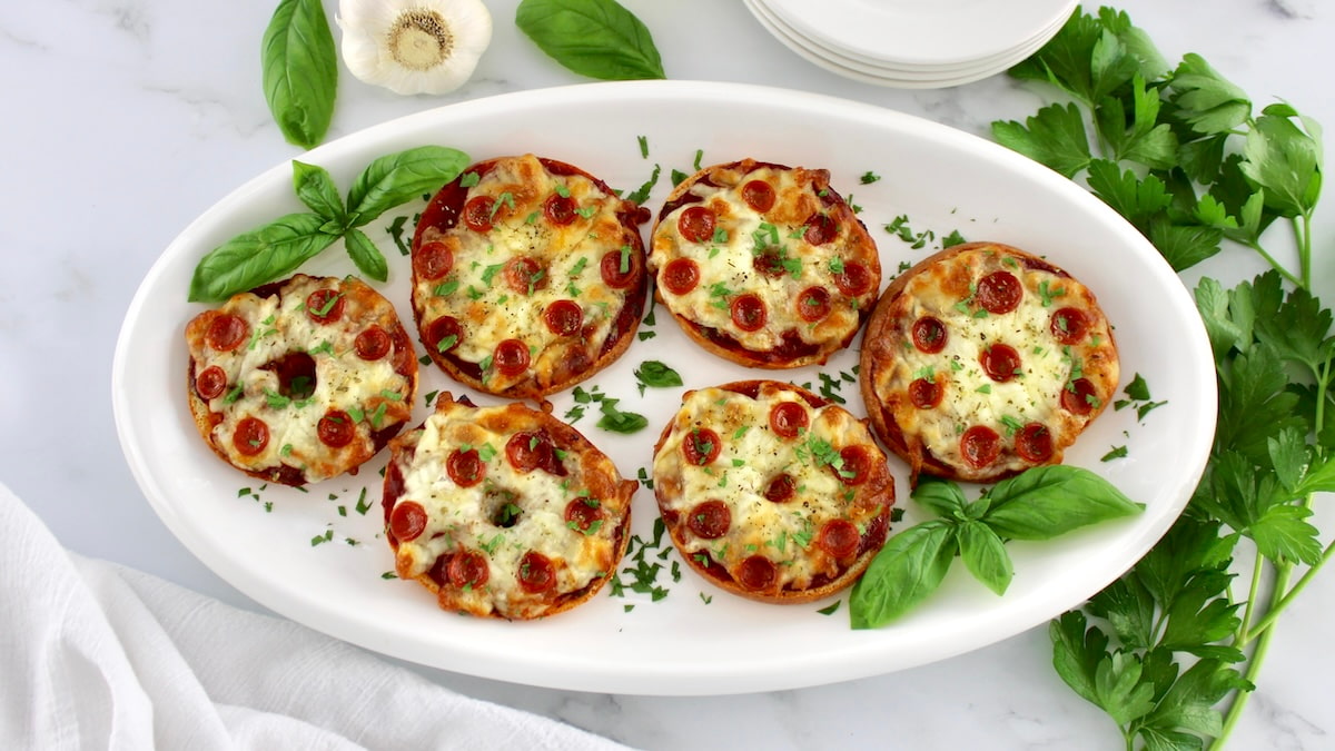 overhead view of Pepperoni Pizza Bagels on white oval platter with fresh basil garnish