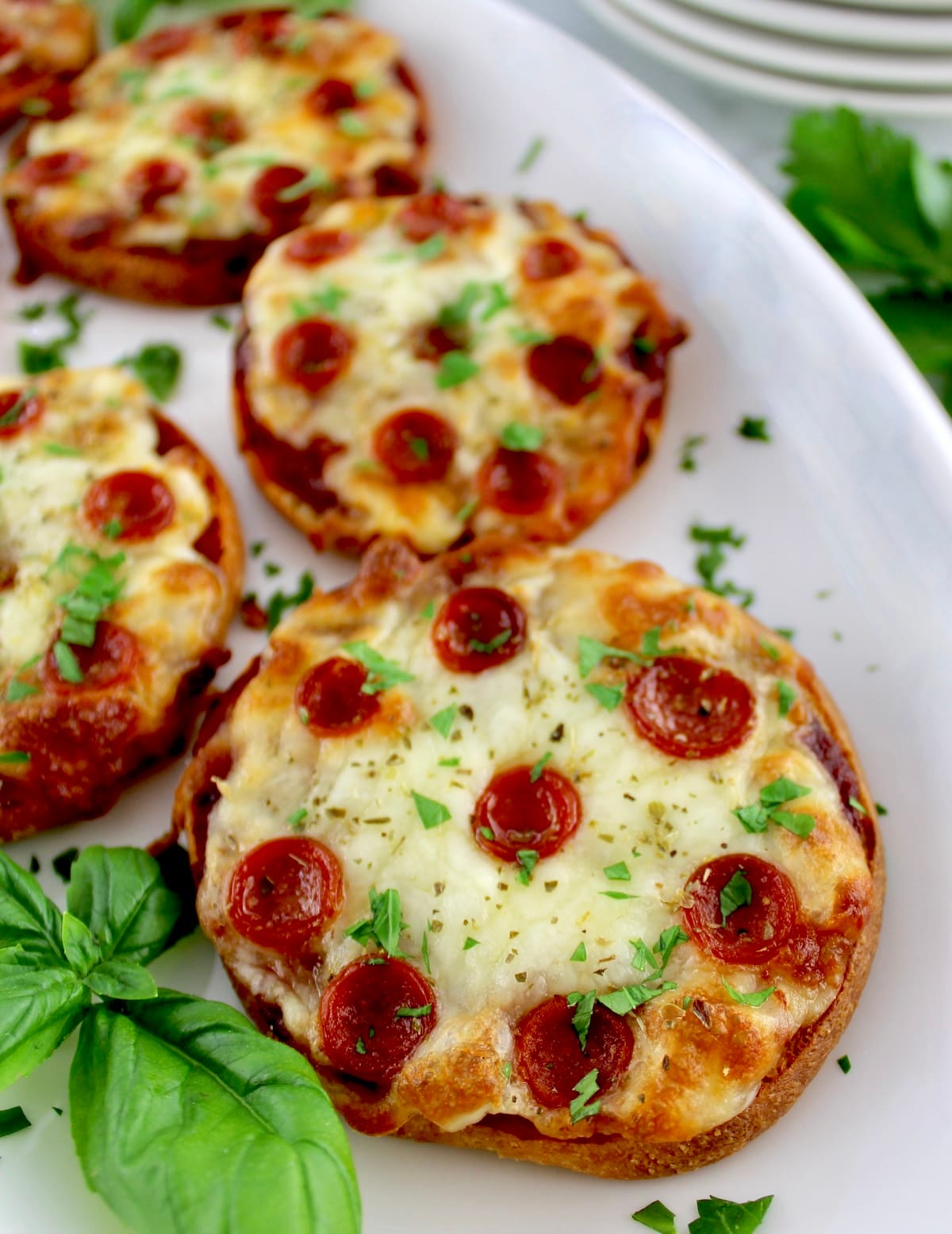 closeup of Pepperoni Pizza Bagels on white plate with fresh basil