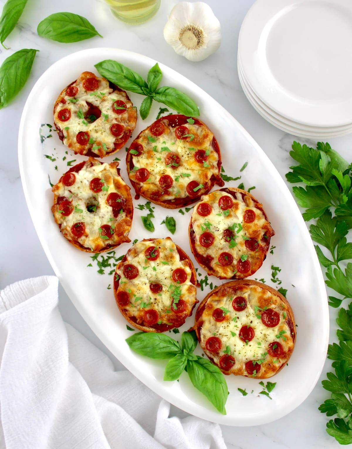 overhead view of Pepperoni Pizza Bagels on white oval plate with fresh bagels