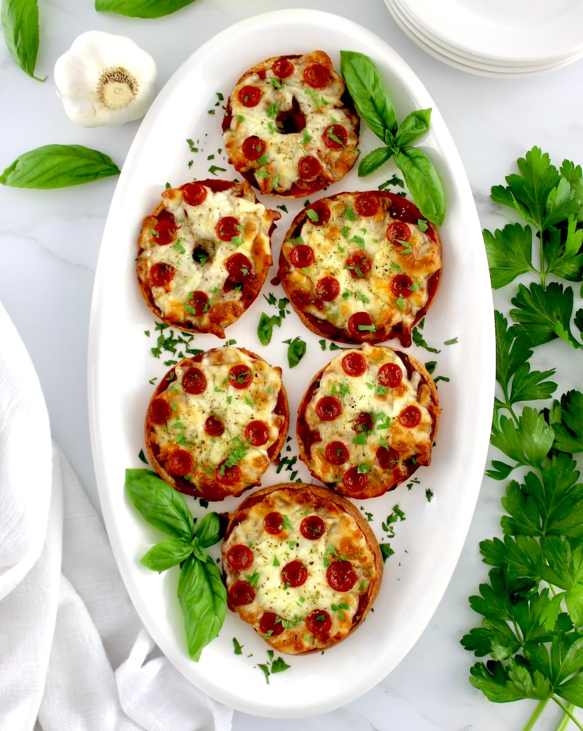 overhead view of Pepperoni Pizza Bagels on white oval platter with fresh basil