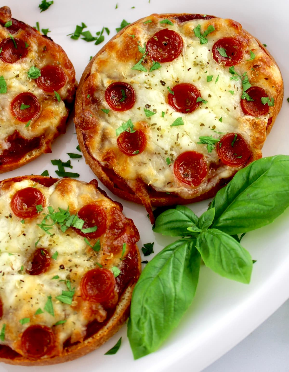 closeup of Pepperoni Pizza Bagels on white plate with fresh basil