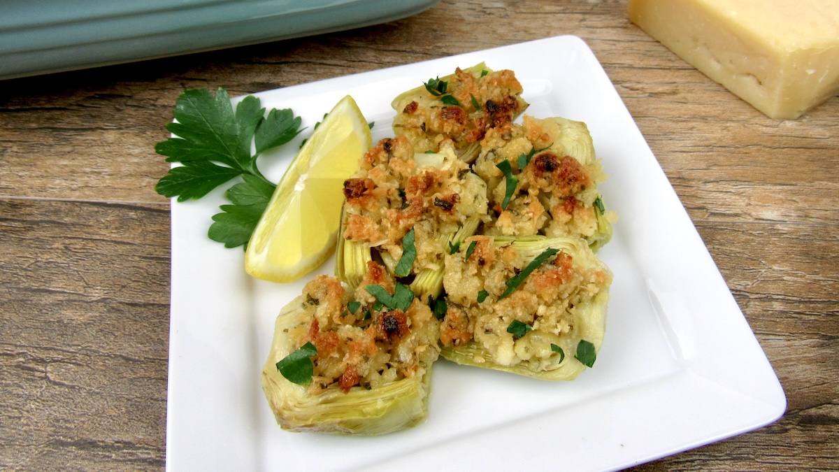 Parmesan Baked Artichoke Hearts on white square plate with lemon slices and parsley on side