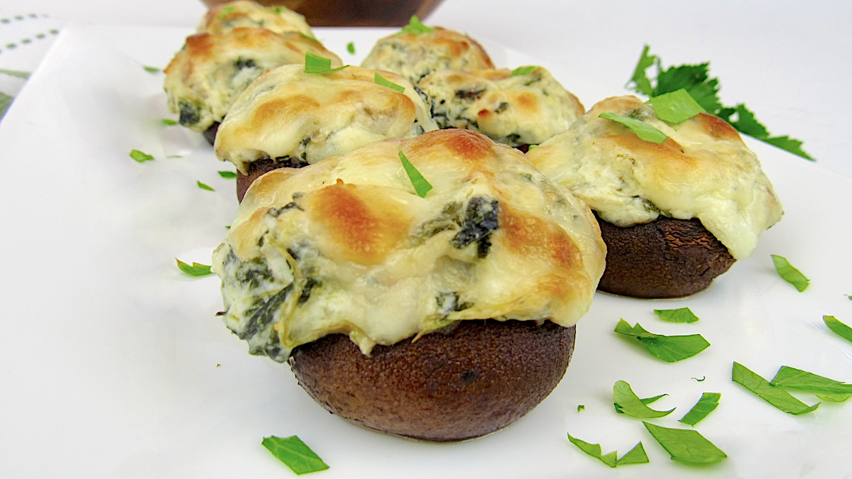 Spinach Artichoke Stuffed Mushrooms on white platter with chopped parsley garnish