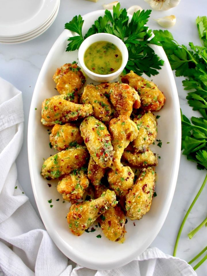 Air Fryer Garlic Parmesan Wings on white oval platter with butter sauce and parsley on side