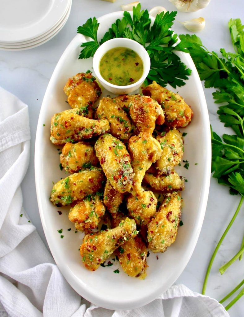Air Fryer Garlic Parmesan Wings on white oval platter with butter sauce and parsley on side