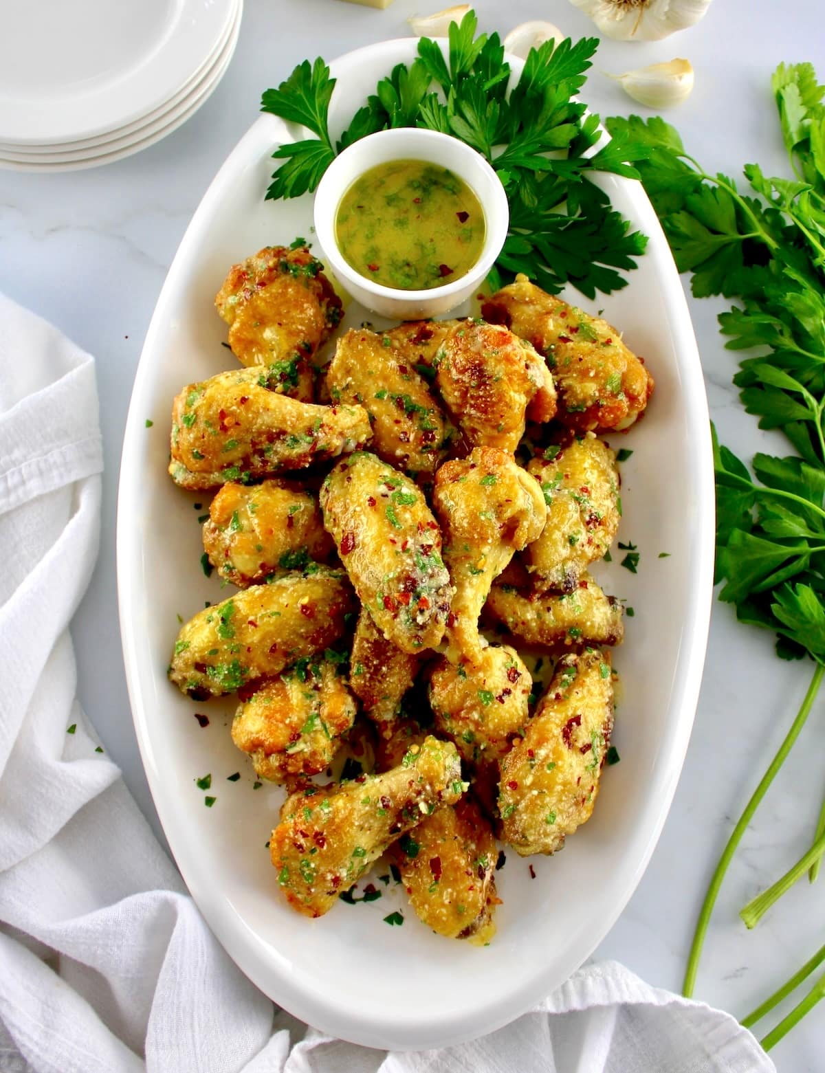 Air Fryer Garlic Parmesan Wings on white oval platter with butter sauce and parsley on side