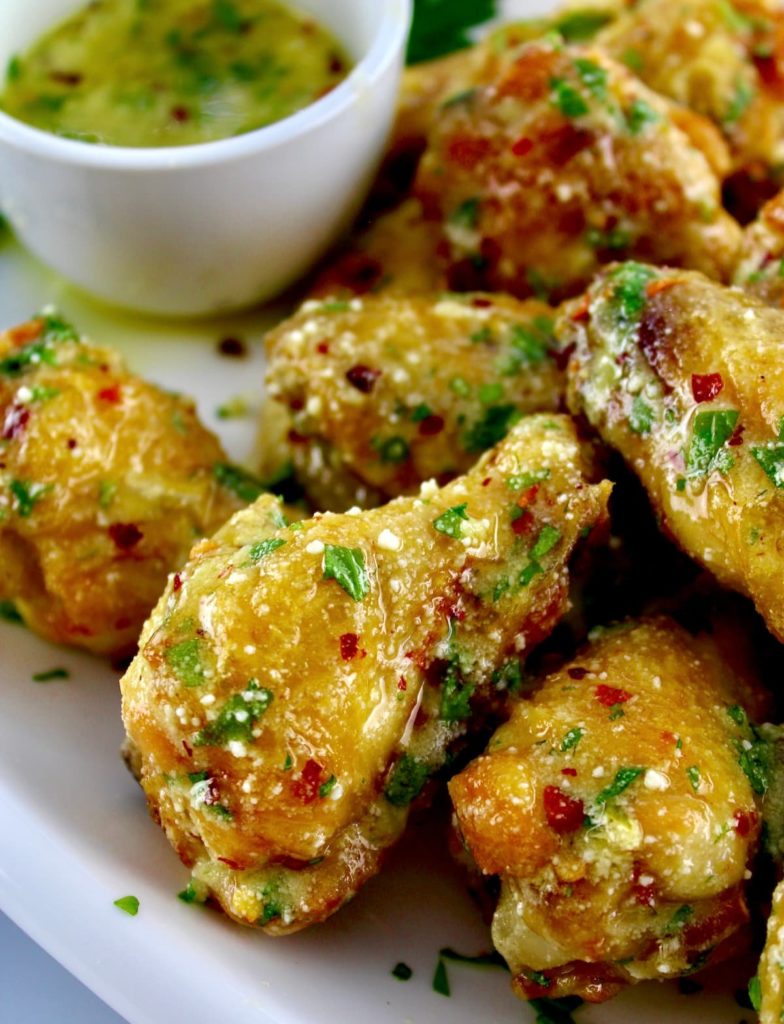 closeup of Air Fryer Garlic Parmesan Wings on white platter with butter sauce in back