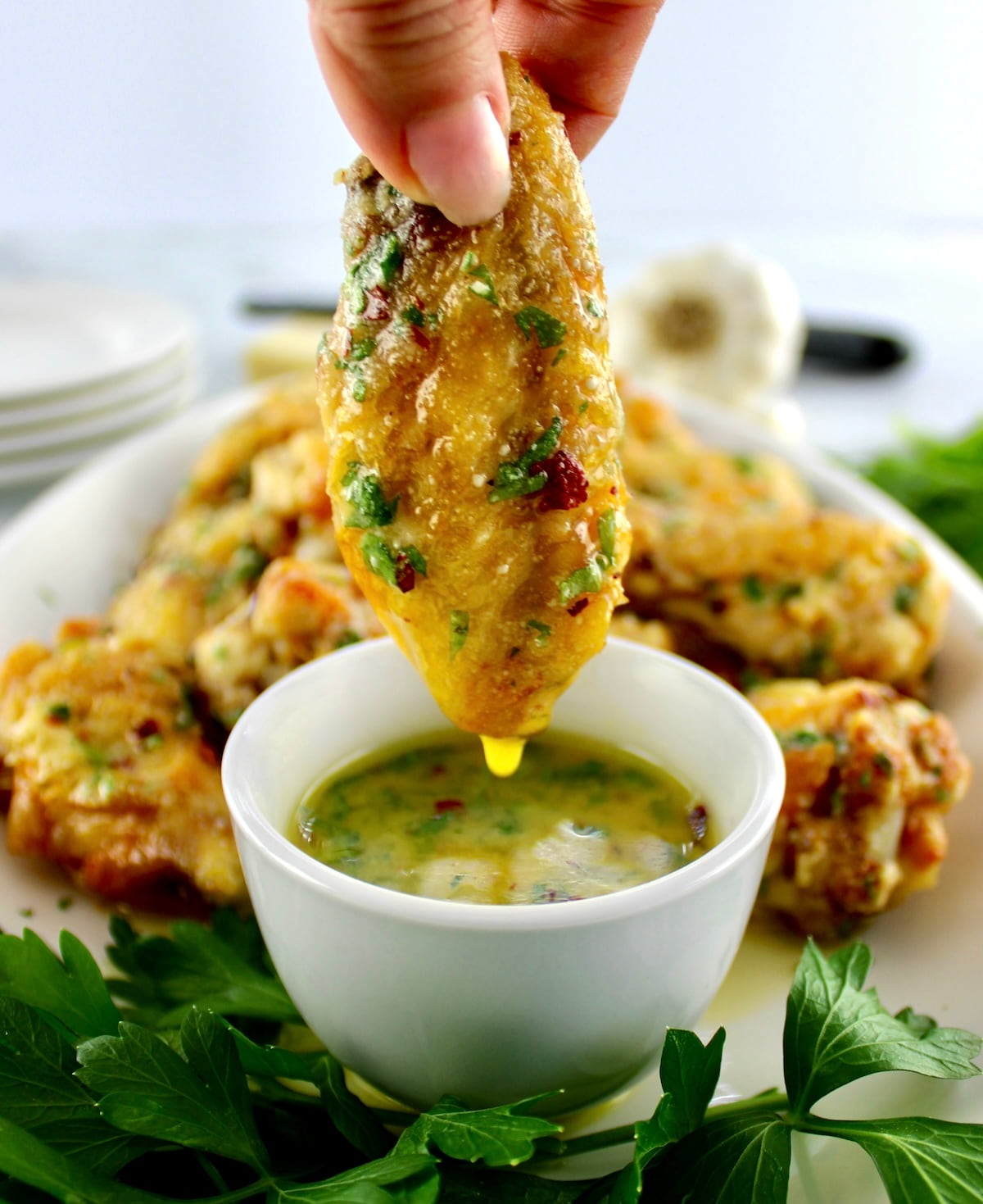 Air Fryer Garlic Parmesan Wing being dipped into butter sauce in white cup and dripping