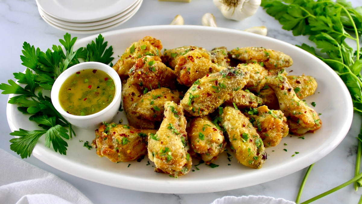 Air Fryer Garlic Parmesan Wings in white oval platter with butter sauce on side and parsley garnish