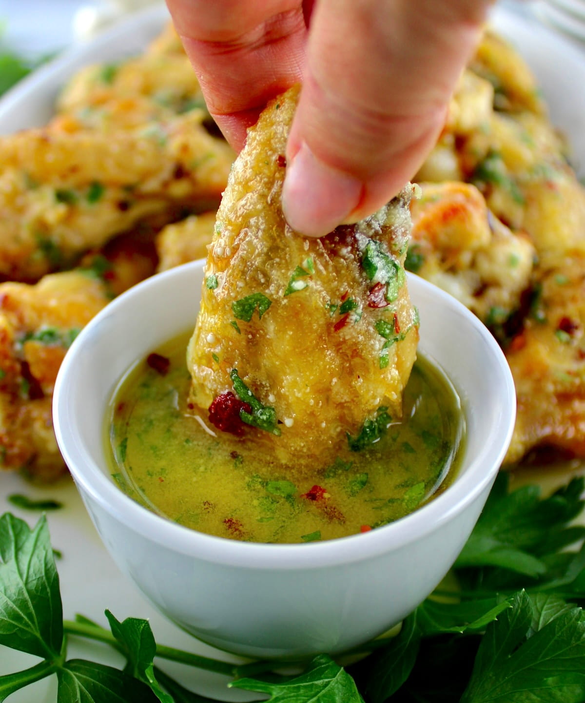 Air Fryer Garlic Parmesan Wing being dipped into butter sauce in white cup